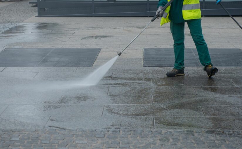 Worker in safety vest pressure washing urban pavement with high-powered water jet