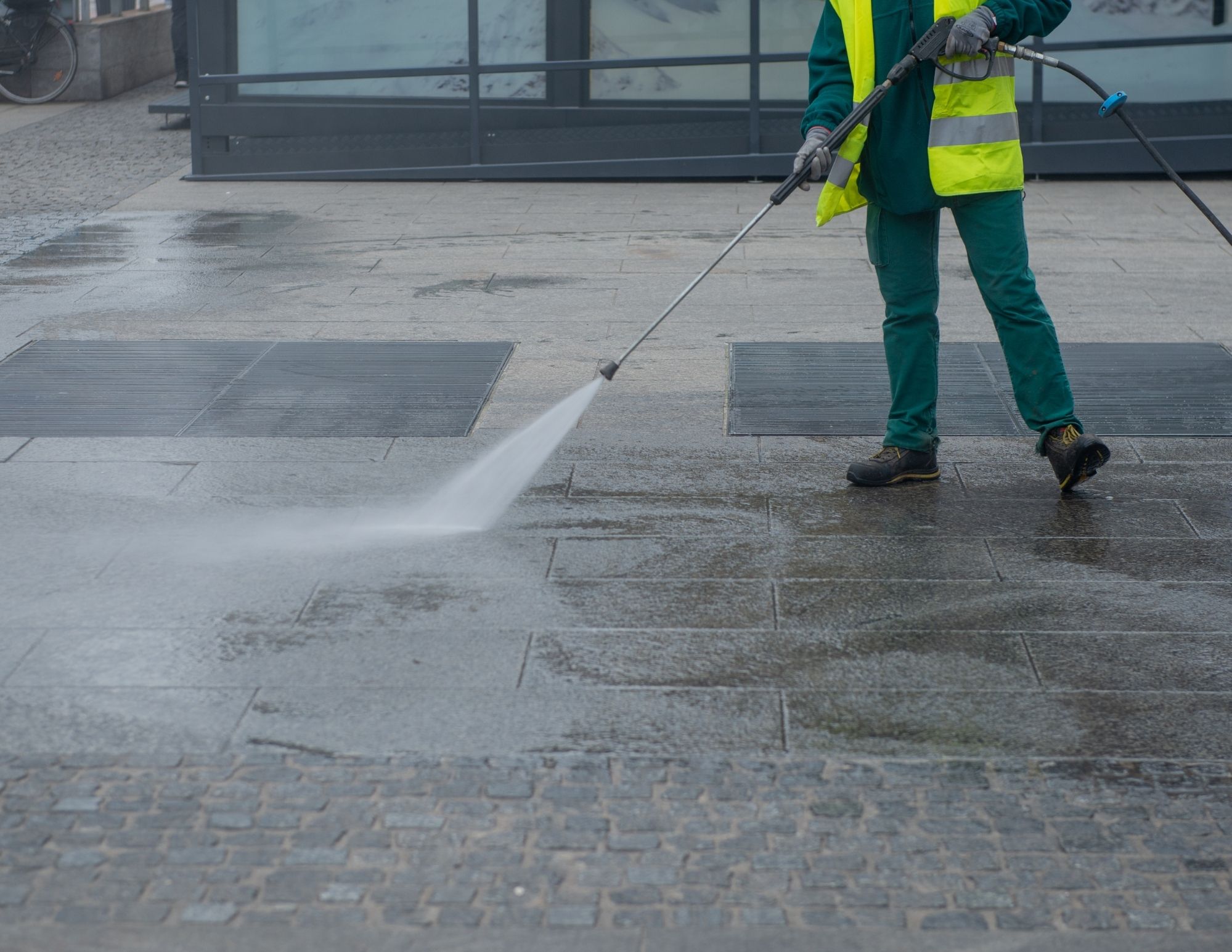 Worker in safety vest pressure washing urban pavement with high-powered water jet