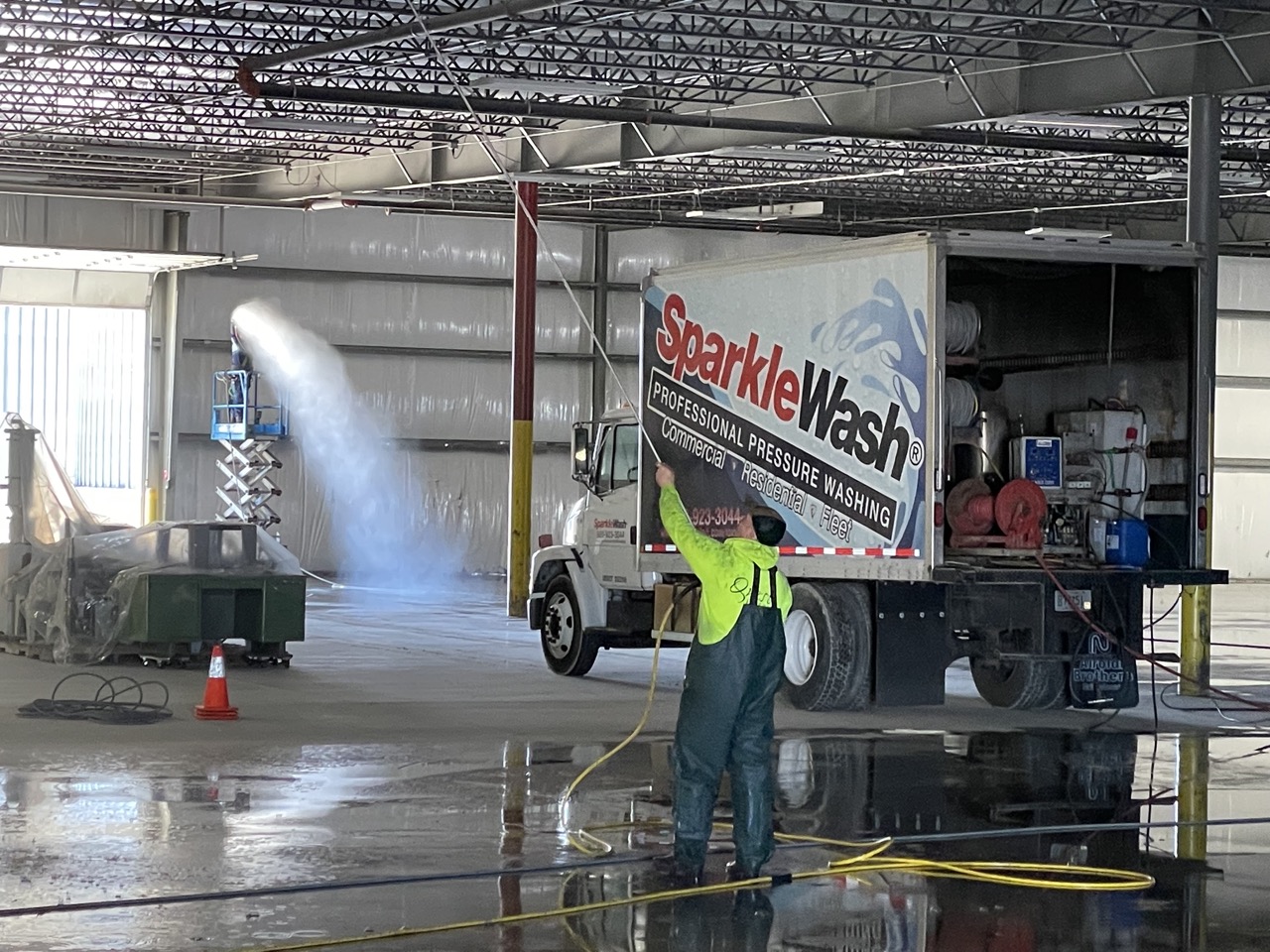 Worker in yellow safety vest operating pressure washing equipment on Sparkle Wash commercial truck inside warehouse facility in Fond du Lac, Wisconsin