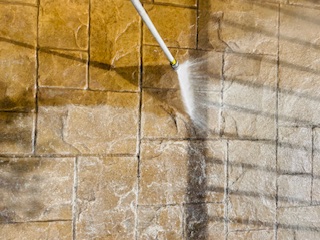 Pressure washing dirty tile wall with white spray nozzle, removing stains and grime from stone surface