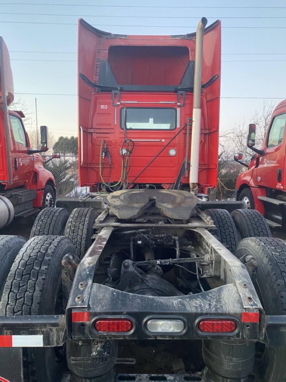 Rear view of a heavy-duty semi truck chassis with dual rear axles and multiple tires parked among other red commercial trucks at a fleet facility in Fond du Lac, Wisconsin