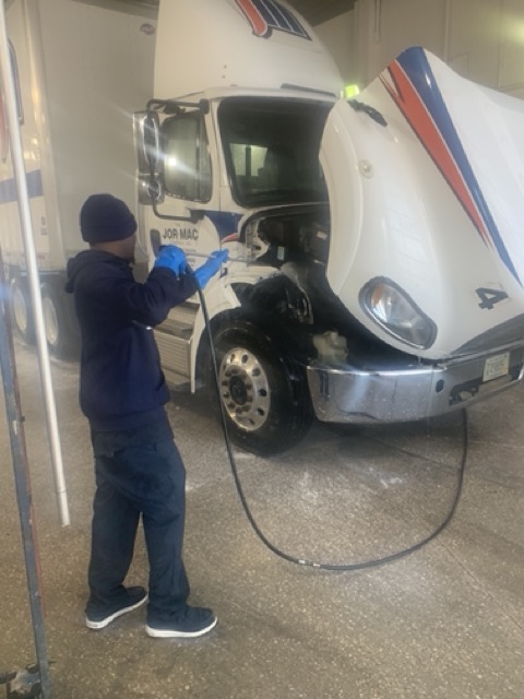 Worker in blue uniform pressure washing white commercial truck with hose in Fond du Lac facility