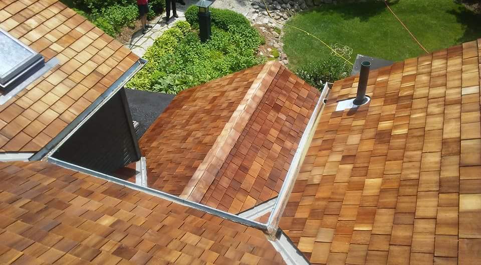 Aerial view of cedar shake roofing with an open skylight well on a residential home in Fond du Lac, showing surrounding shingled roofs and green lawn below