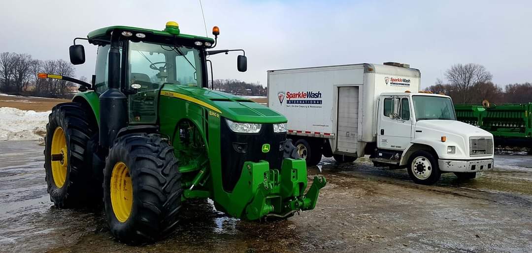 Green John Deere tractor with yellow rims parked next to white SparkleWash service truck at Fond du Lac pressure washing facility