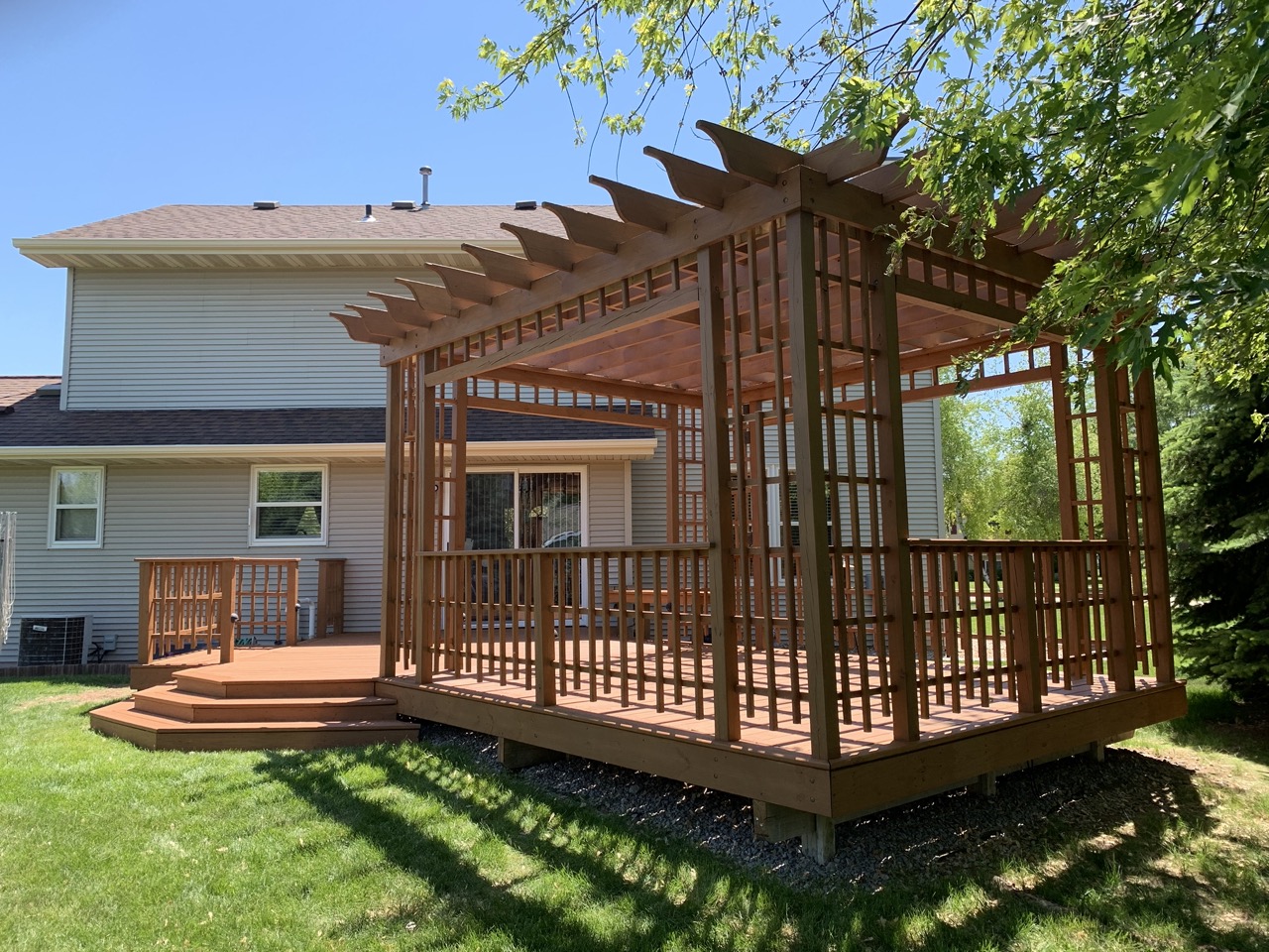 Wooden pergola and deck attached to a two-story house with landscaped yard in Fond du Lac, Wisconsin