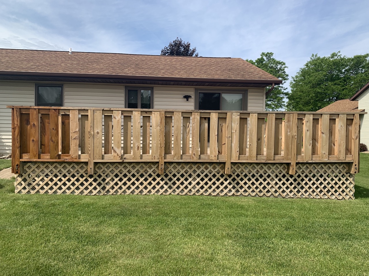 Wooden deck with lattice skirting attached to beige house with three windows, surrounded by green lawn in Fond du Lac, Wisconsin