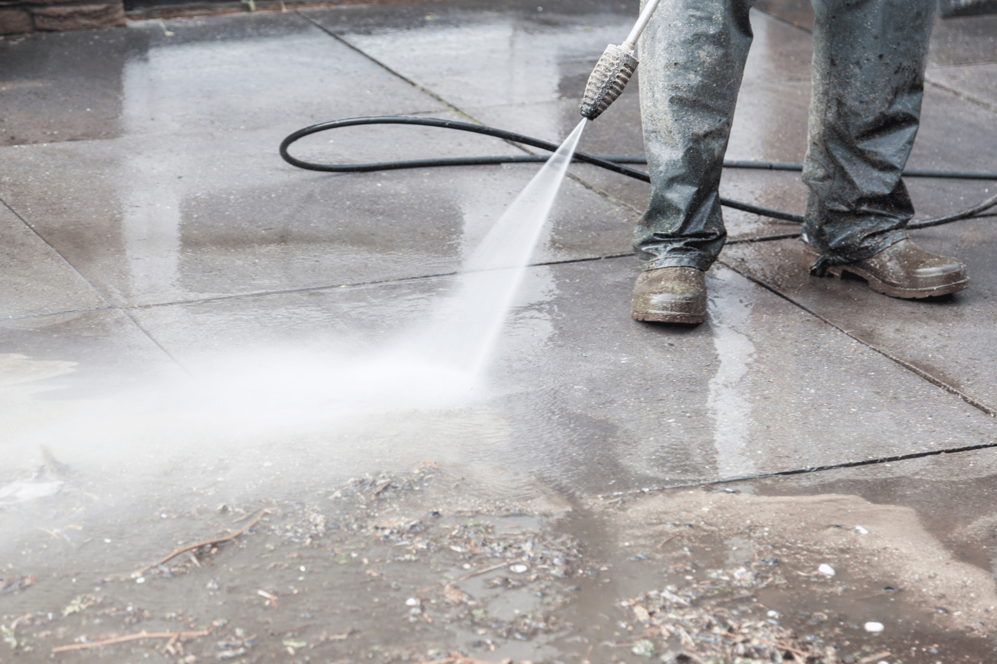 Worker pressure washing concrete dumpster pad in Fond du Lac, Wisconsin, removing dirt and debris with high-pressure cleaning equipment