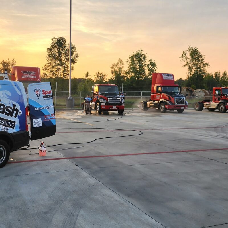 Sparkle Wash professional pressure washing service vehicle parked beside a fleet of red trucks at a commercial washing facility in Texarkana during sunset