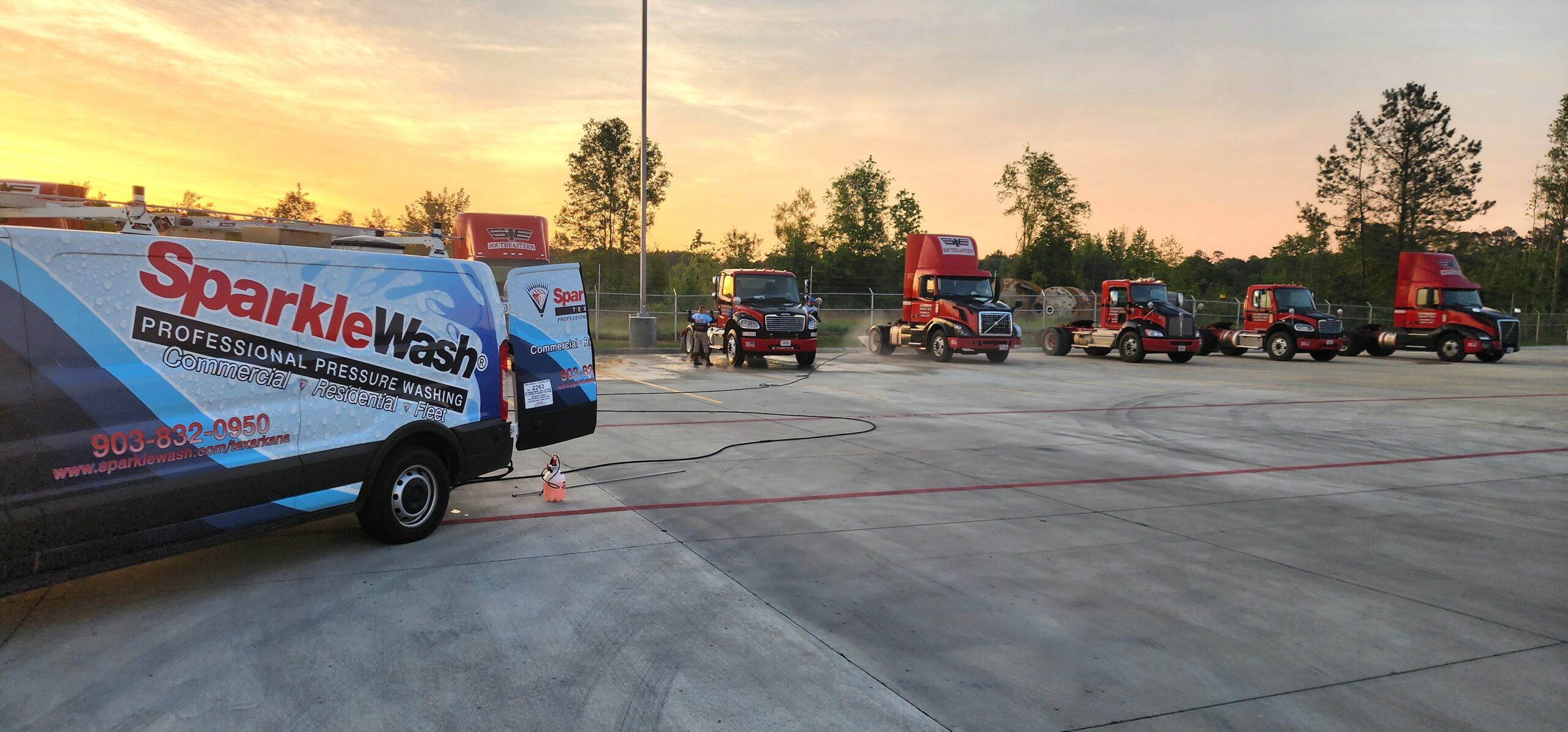 Sparkle Wash professional pressure washing service vehicle parked beside a fleet of red trucks at a commercial washing facility in Texarkana during sunset