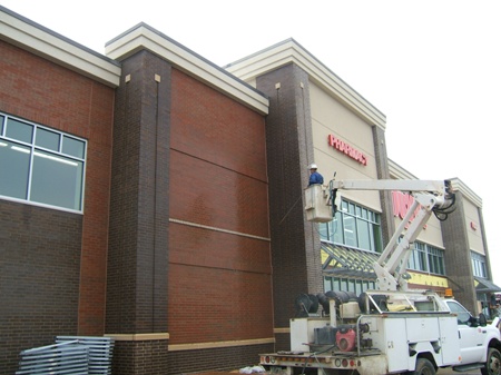 Commercial storefront building exterior cleaning in progress with pressure washing equipment and lift in Fond du Lac, Wisconsin