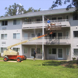 Three-story apartment complex in Fond du Lac undergoing exterior pressure washing and house cleaning services, with equipment and truck visible on the lawn
