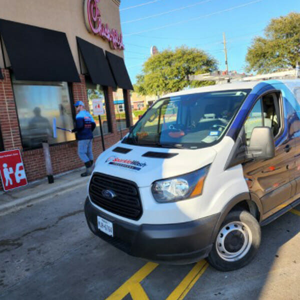 White Ford Transit van with pressure washing company branding parked on yellow lines outside brick storefront in Fond du Lac, Wisconsin